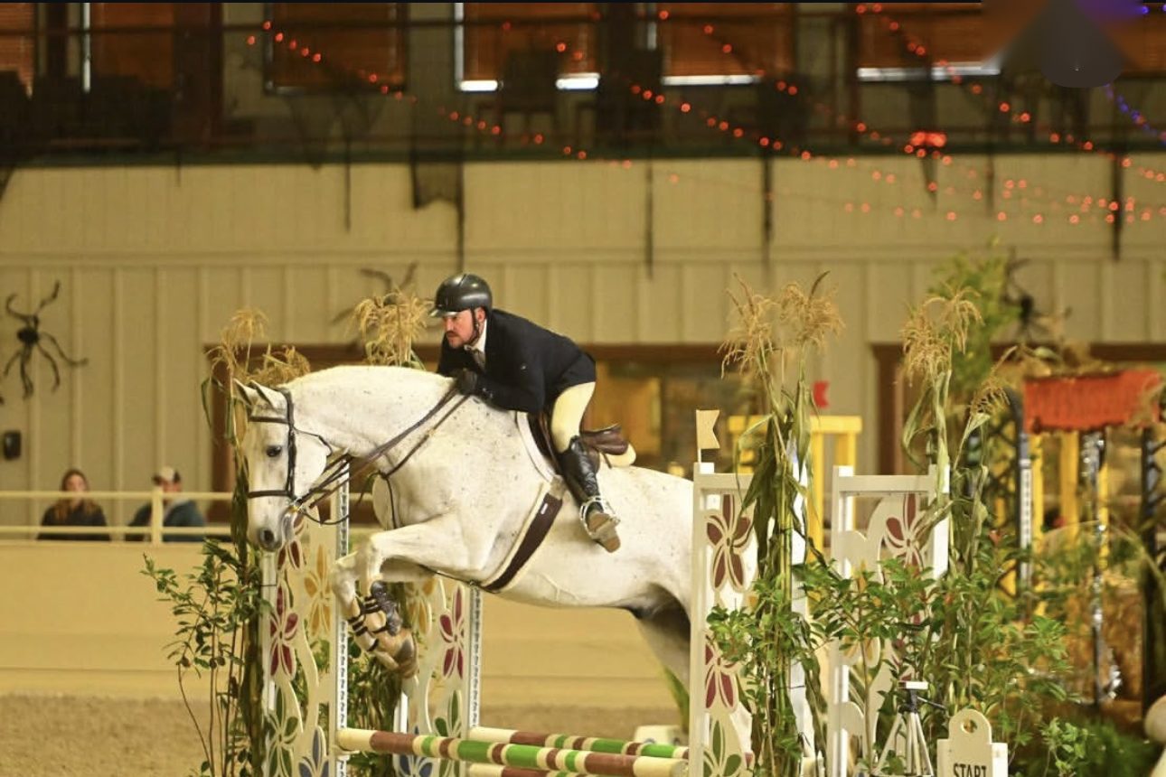 Ryan Oropeza riding Rendezvous in an indoor arena, jumping a decorated hunter fence