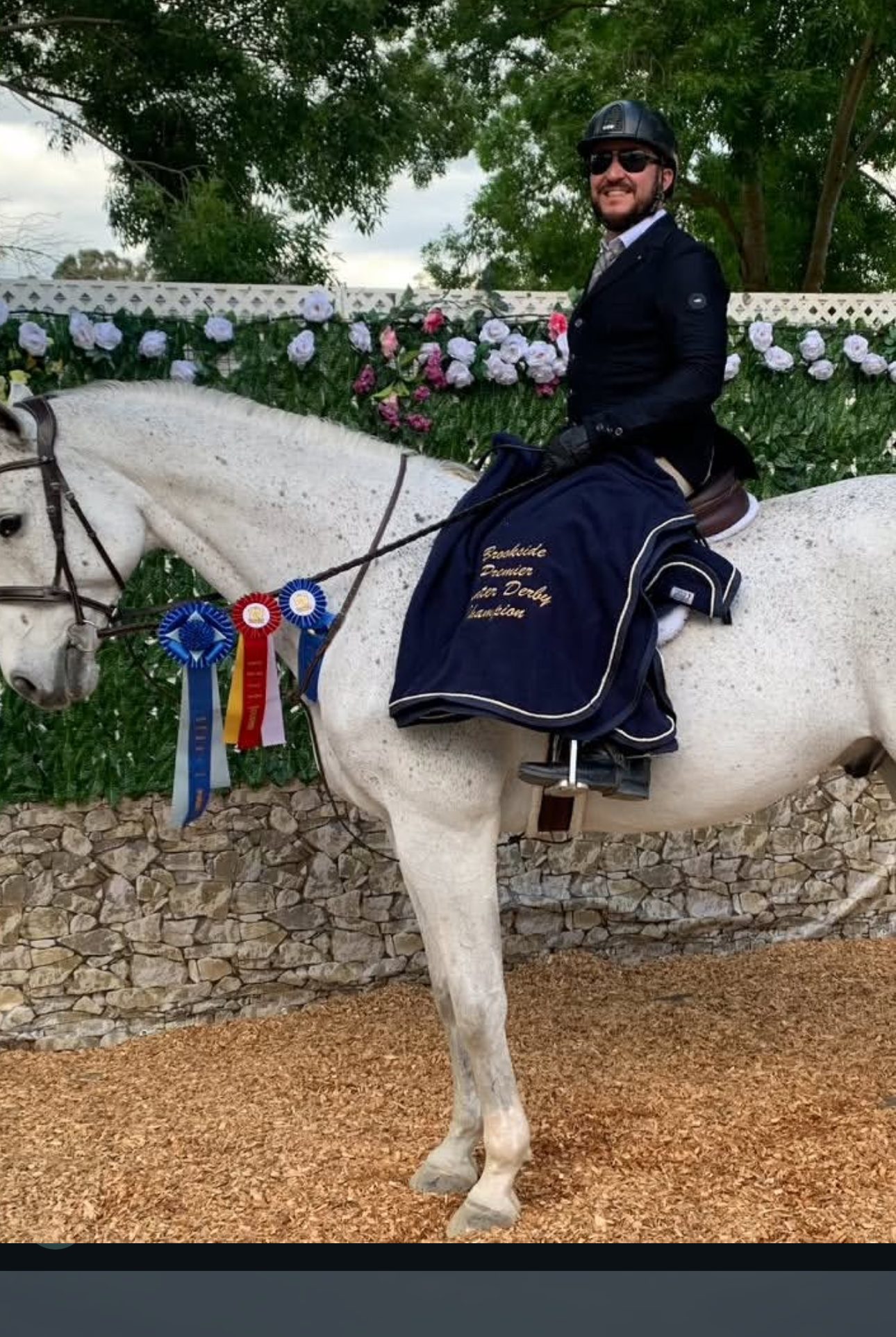 Ryan Oropeza on his Silver Gray, Rendezvous, after winning the Brookside Premier Derby — three rosettes on the bridle and a navy 'Brookside Premier Derby Champion' cooler on the horse's hindquarters
